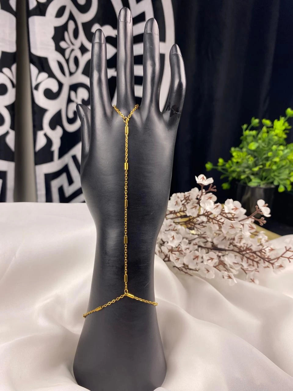 Gold chain bracelet on a black mannequin hand with a decorative background