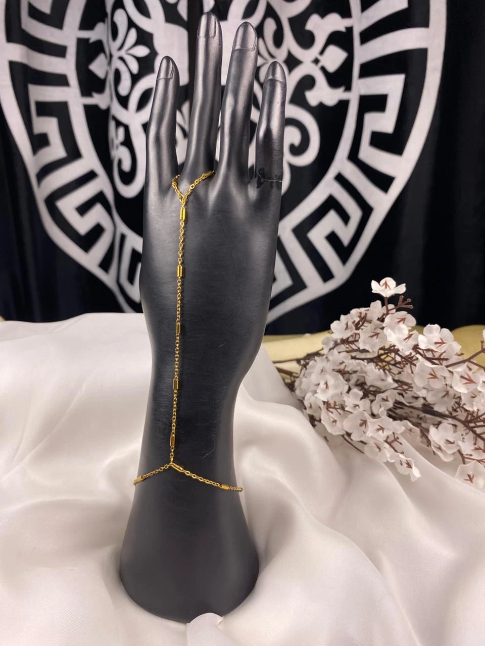 Gold body chain on a black mannequin hand with a decorative background