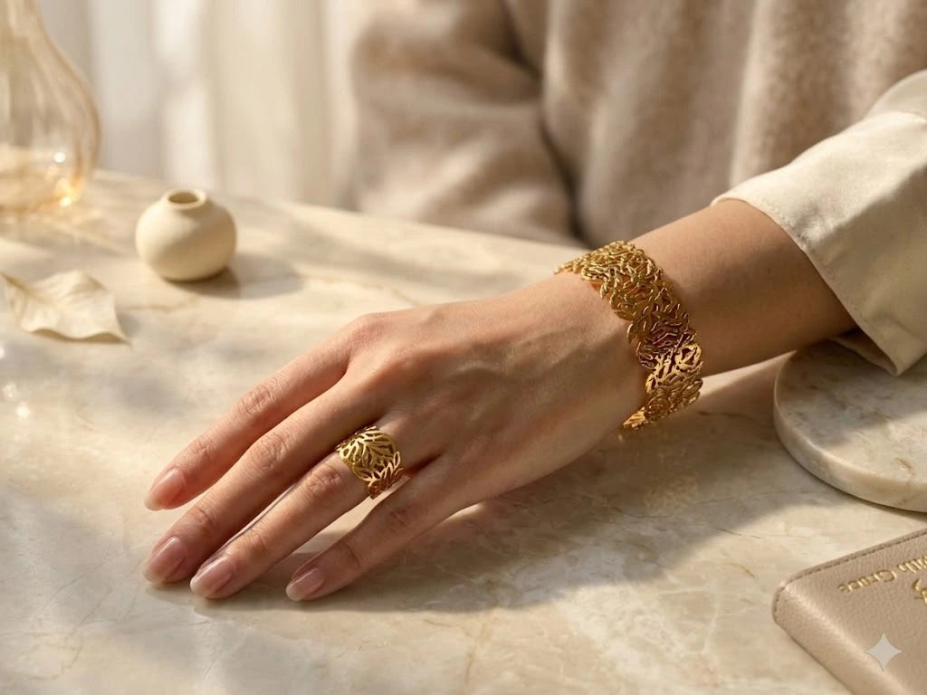 Hand wearing a gold ring and bracelet on a marble surface with soft lighting