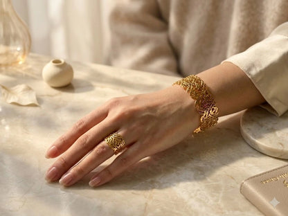 Hand wearing a gold ring and bracelet on a marble surface with soft lighting