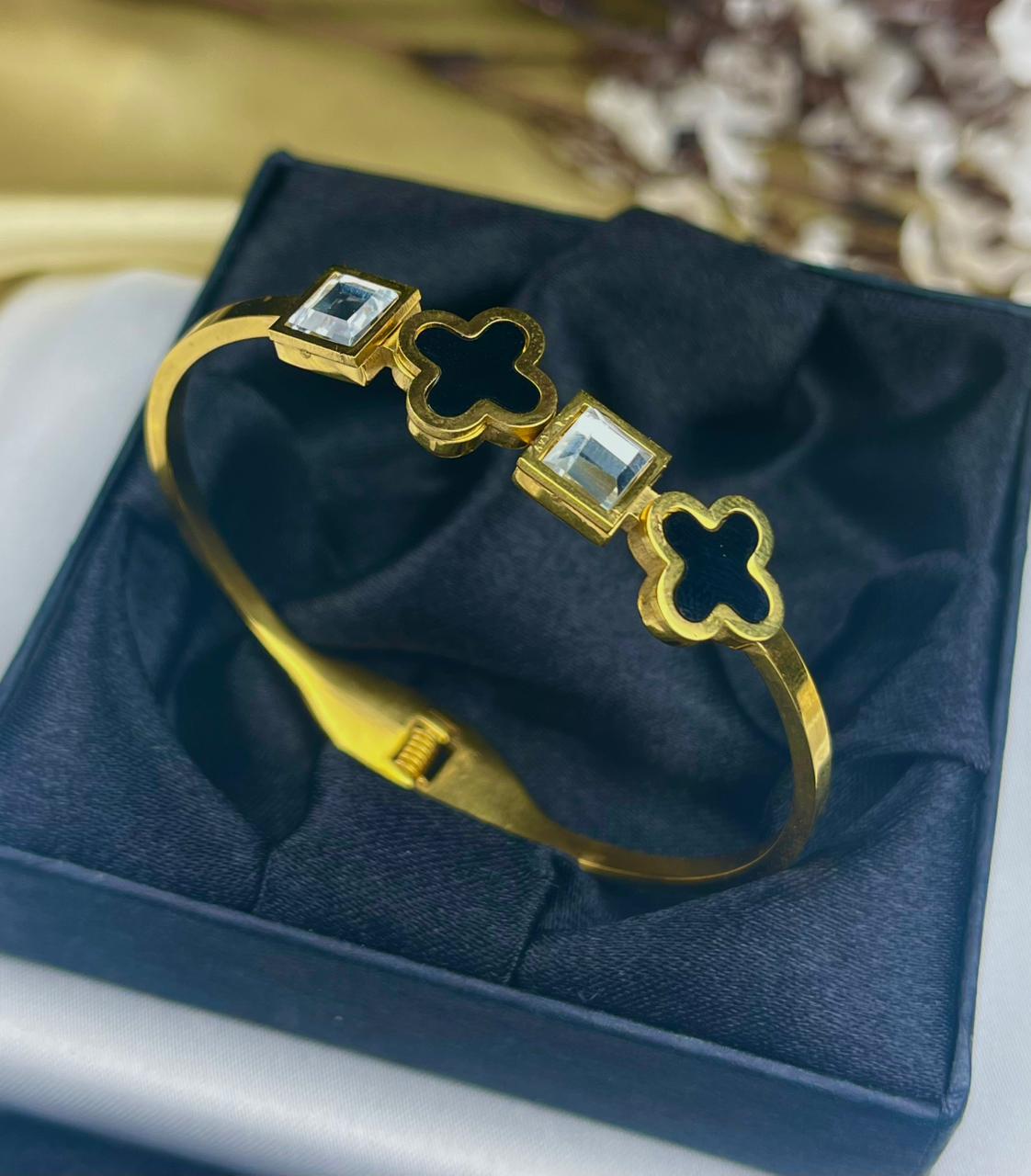 Gold bracelet with clover designs and gemstones on a blue cushion
